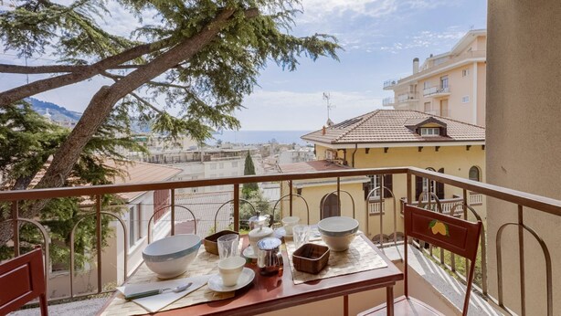 A balcony with a table set for dining, overlooking a cityscape and the sea. - GuestHost - Cozy apartment of about 110 square meters, able to accommodate up to 5 people, located on the 2nd floor of a building with lift and garage.The apartment has an enchanting view of the sea and the marina, surrounded by the greenery of Villa Orm (Sanremo)