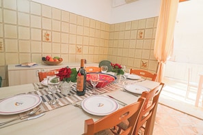 Un coin repas agrémenté d’un mur recouvert de carreaux, une table mise pour quatre personnes avec des assiettes, des verres et une bouteille de vin.