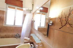 Une salle de bain avec une baignoire, un rideau de douche, un miroir et une fenêtre.