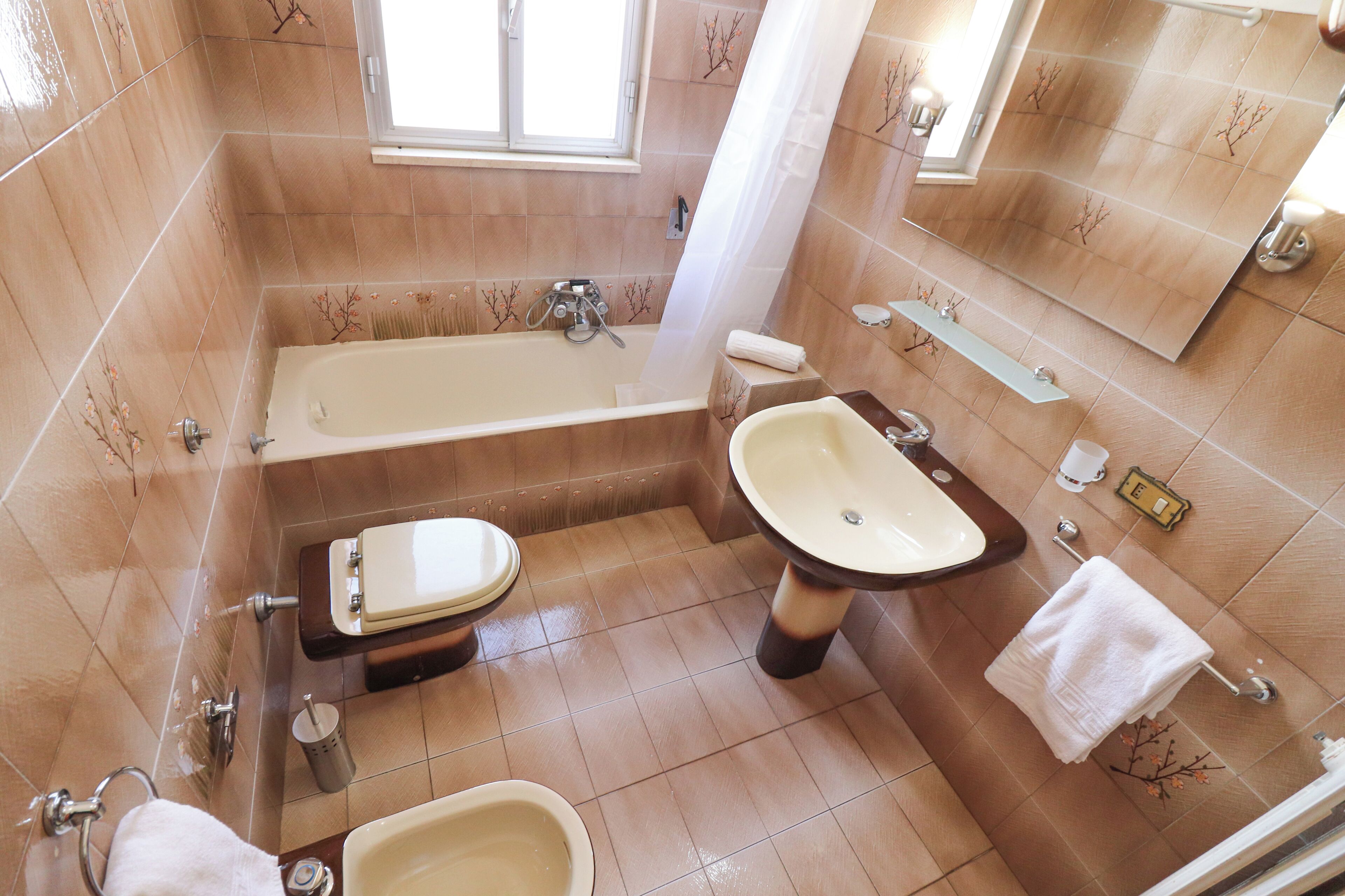 A bathroom with a bathtub, toilet, and sink, all with matching brown tiles and a window above the bathtub.