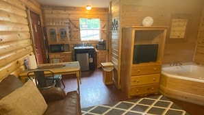 A cozy cabin interior with a wooden interior, a dining area, a kitchenette, a fireplace, and a large window.