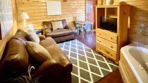 A cozy log cabin interior with a wooden ceiling, a ceiling fan, a sofa, a TV, and a bathtub.
