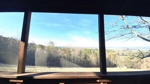 A wooden deck with a view of a forested landscape through large windows.