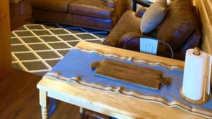 A cozy cabin interior with a wooden floor, a leather sofa, a dining table with a placemat, and a ceiling fan.