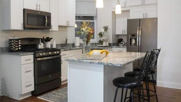 A modern kitchen with white cabinets, a stainless steel refrigerator, a built-in oven, and a central island with bar stools.