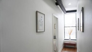 A hallway with white walls, a wooden floor, and a window with blinds.