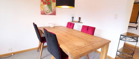 Un comedor con una mesa de madera, sillas negras y rojas, una lámpara negra y un cuadro de flores en la pared.