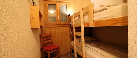 Ein kleiner, gemütlicher Raum mit einem Etagenbett, einem Holzhocker mit rotem Kissen und einem kleinen Schrank mit Spiegel.