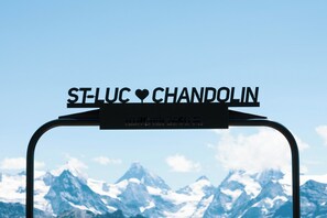 Ein Metallschild mit 'ST-LUC CHANDOLIN' und einem Herzsymbol vor einer Bergkulisse.