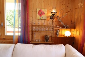 Una habitación acogedora con una pared de madera, un cuadro de flores, una estantería con copas, una lámpara y una decoración con forma de estrella.