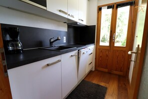 A compact kitchen with white cabinets, a black countertop, a coffee maker, and a wooden door with a window.