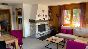 A cozy living room with a stone fireplace, a sofa, a coffee table, and a dining area with chairs.
