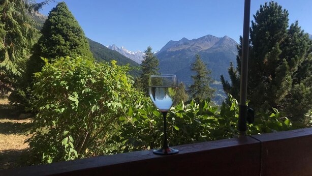 A glass of water on a balcony with a view of mountains and trees.