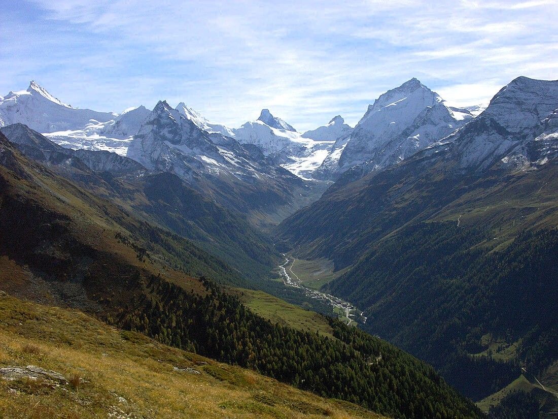 A mountainous landscape with snow-capped peaks, a valley, and a river.