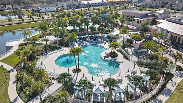A resort with a large central pool, surrounded by palm trees and lounge chairs.