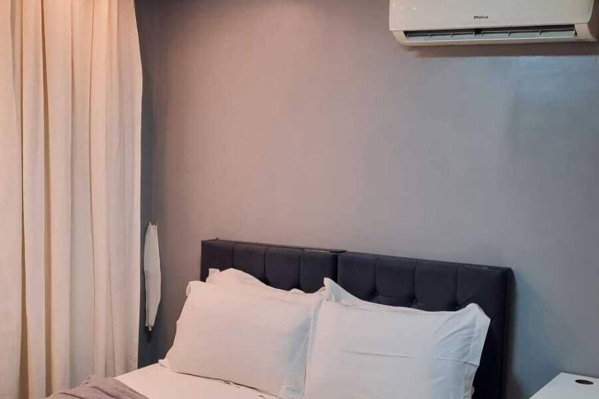 Hotellihuone, jossa on sänky, yöpöytä, ilmastointilaite ja ikkuna, jossa on verhot.