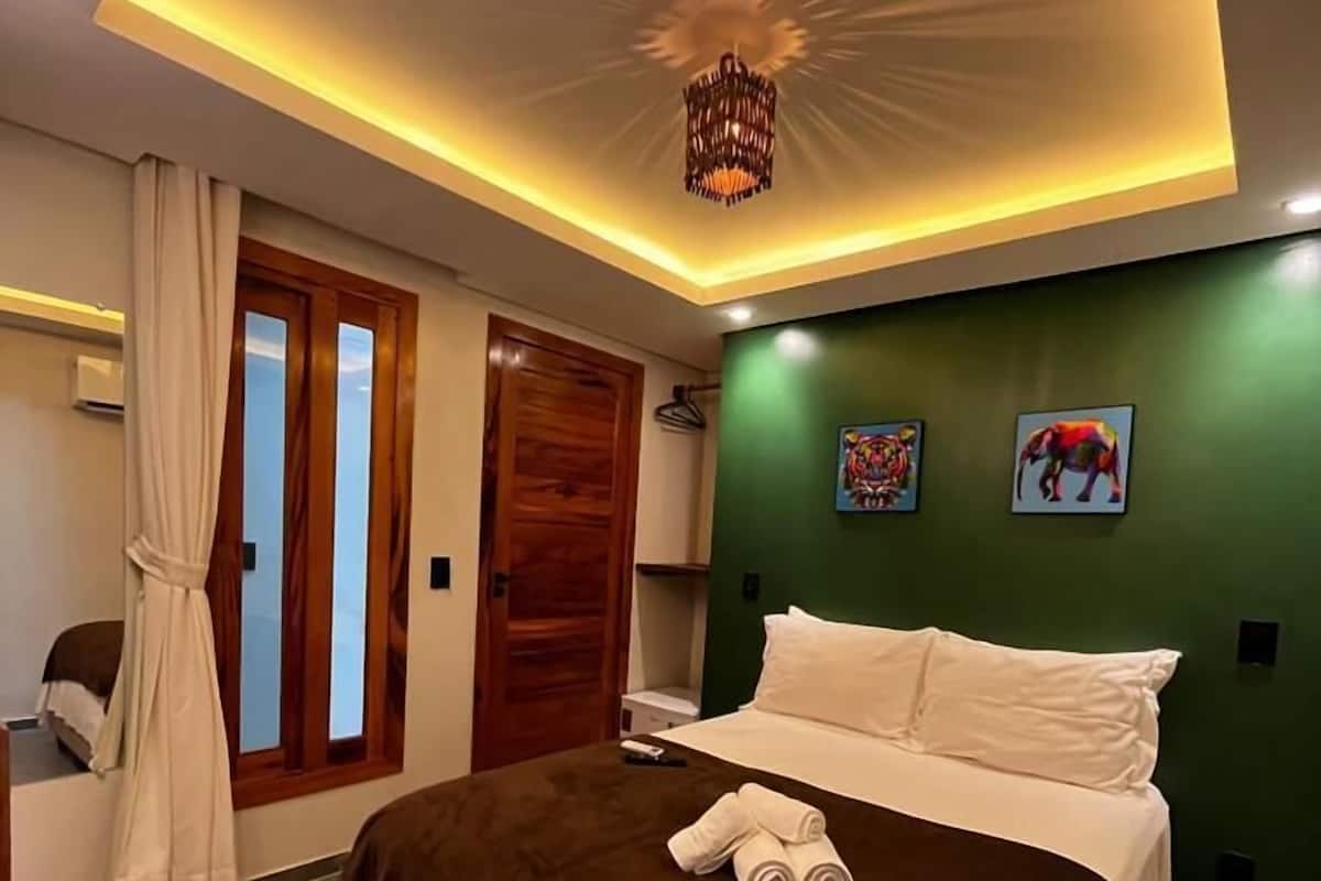 Moderni hotellihuone, jossa on suuri sänky, vihreä tehosteseinä ja kattovalaisin.
