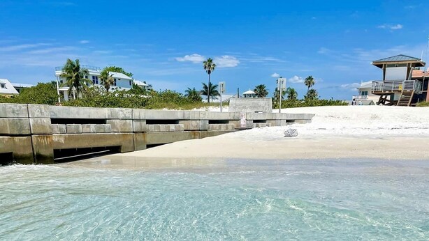 Una playa despejada con arena y un muro de concreto.