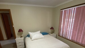 Een slaapkamer met een bed, twee nachtkastjes, een lamp, en een raam met jaloezieën.