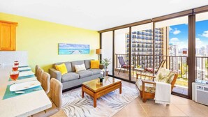 Ein modernes Wohnzimmer mit Sofa, Couchtisch und Sesseln, ein Essbereich mit Tisch und Stühlen sowie ein großer Balkon mit Blick auf die Stadt.