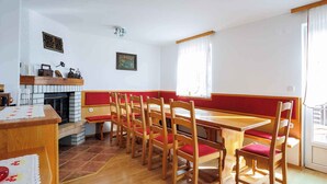 Un espace repas avec des chaises et des bancs en bois, une cheminée et une fenêtre avec des rideaux.