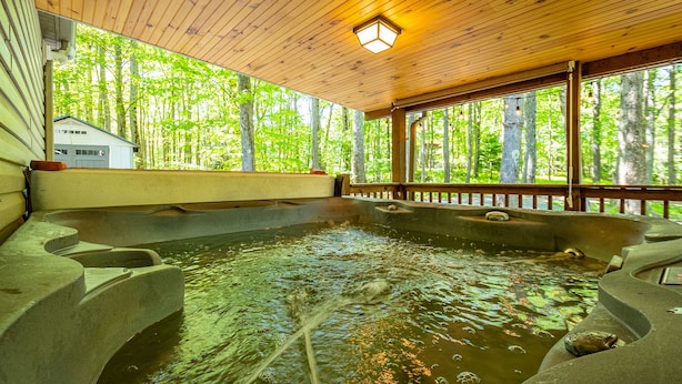 Eine Holzterrasse mit Whirlpool, umgeben von Steintreppen, mit Blick auf einen bewaldeten Bereich.