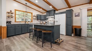 Eine moderne Küche mit dunkelgrauen Schränken, einer zentralen Kochinsel mit Sitzgelegenheiten, einem eingebauten Backofen und einem Kühlschrank.