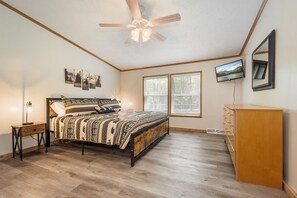 A bedroom with a bed, a nightstand, a dresser, a ceiling fan, and two windows.