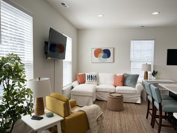 Una sala moderna con un conjunto de sofás, un televisor montado en la pared y un comedor con sillas y una mesa.