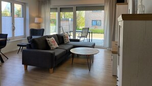 A modern living room with a sofa, armchairs, and a coffee table. There is a sliding glass door leading to a patio area with outdoor furniture. - Strandwiese - Ankerplatz - Ankerplatz - Strandnah... Wellenrauschen Inklusive! (Dahme)