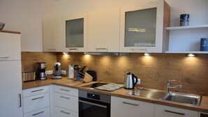 A modern kitchen with white cabinets, a stainless steel sink, a coffee maker, and a kettle. - Strandwiese - Ankerplatz - Ankerplatz - Strandnah... Wellenrauschen Inklusive! (Dahme)