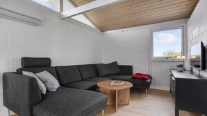 En moderne stue med en grå hjørnesofa, et rundt træsofabord og et fjernsyn på et sort skab.