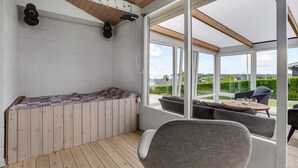 Et solrum med trægulv, et opholdsområde med sofa og stole, samt udsigt til det fri.
