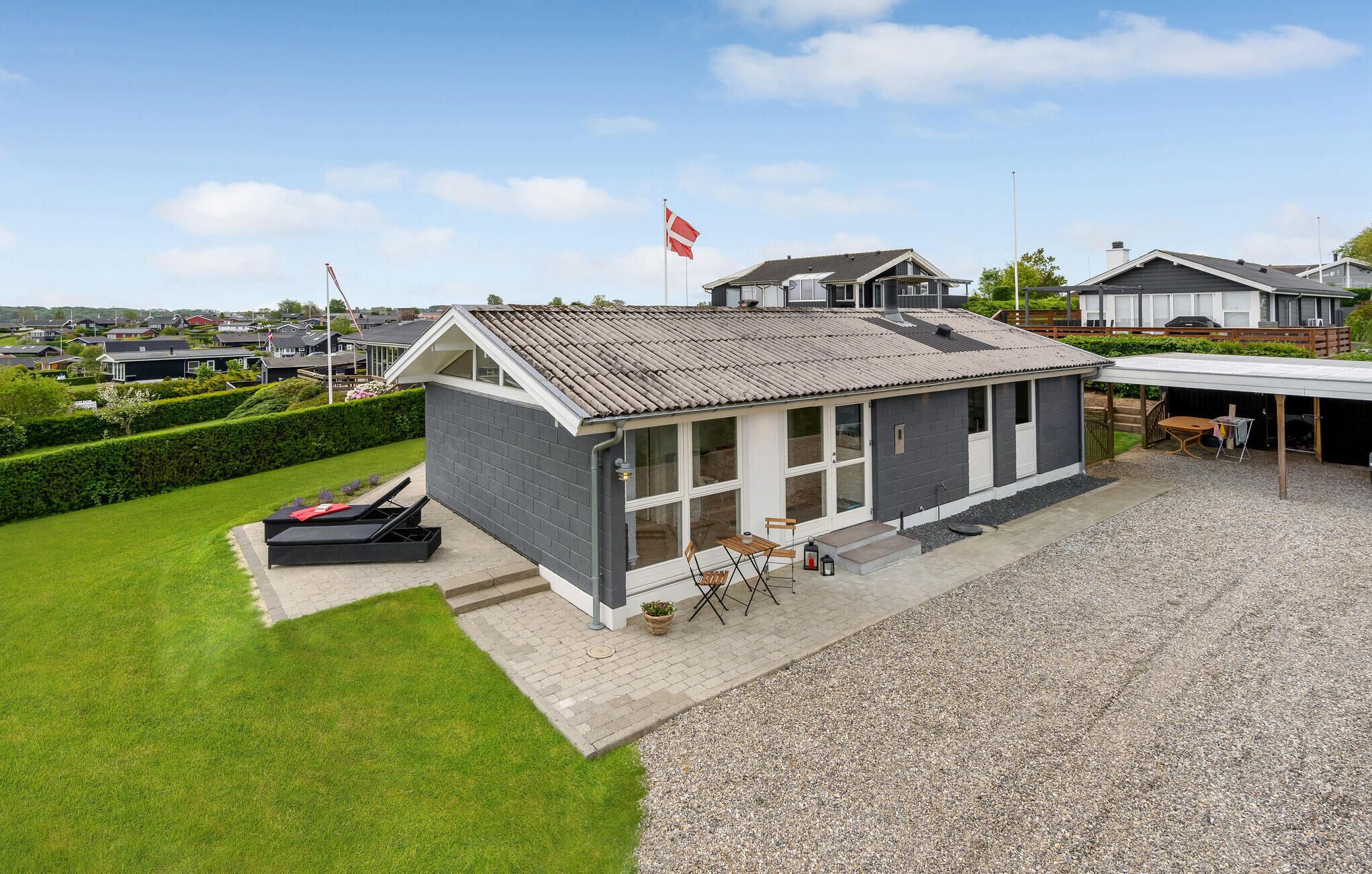 A modern house with a grey exterior, large windows, and a flag on the roof.