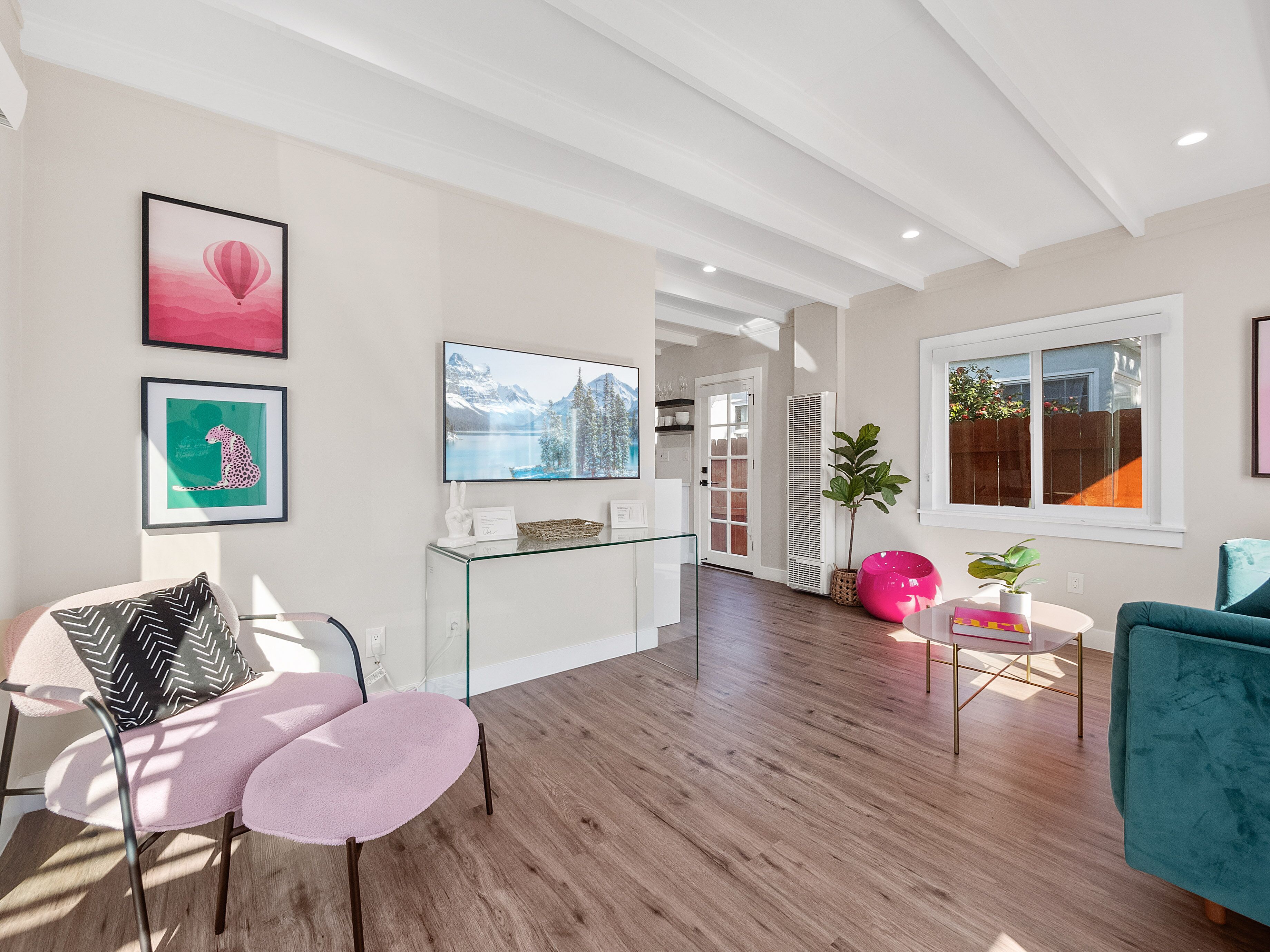 A modern living room with a glass coffee table, a teal sofa, and a pink chair.