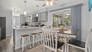 Een moderne keuken met een centraal eiland, barkrukken en een eettafel met stoelen.