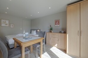 A small, well-lit room with a bed, a desk with a chair, a wardrobe, and a bedside table with a lamp and a bottle. - Appartement Muschel - Haus Neptun - Appartement Muschel (Sylt)