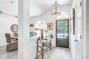 A dining area with a glass table and wicker chairs, a chandelier, and a door leading outside.