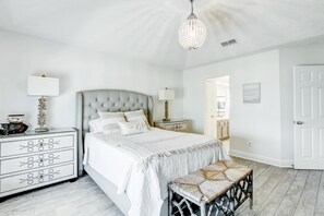 A bedroom with a large bed, bedside tables, a bench, and a chandelier.