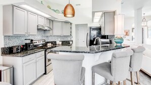 Una cocina moderna con armarios blancos, encimera de granito y una isla central con taburetes de bar.