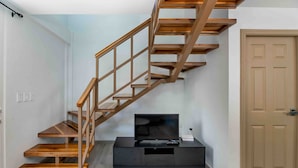 A staircase with wooden steps and a metal railing, leading to a dark-colored entertainment unit with a flat-screen TV and remote control.