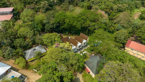 A large house surrounded by dense greenery, with a visible swimming pool and a tennis court.