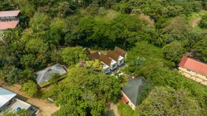 A large house surrounded by dense greenery, with a visible swimming pool and a tennis court. - Cozy Beach Villa at The Shores 5 minutes from the beach (West End)