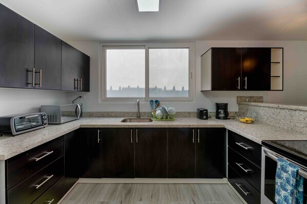 A modern kitchen with dark cabinets, a double sink, and a large window. - Cozy Beach Villa at The Shores 5 minutes from the beach (West End)