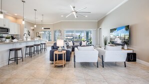 A spacious living area with a kitchen, a dining area, and a large window offering a view of the outdoors. - Sauna, Paddle Boards, Gulf Access, Heated Pool - Villa Sun Kissed - Roelens Vacations (Cape Coral)