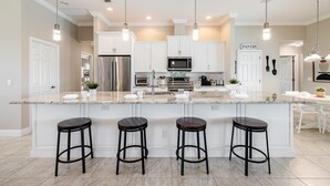 A modern kitchen with white cabinets, stainless steel appliances, and a large island with bar stools. - Sauna, Paddle Boards, Gulf Access, Heated Pool - Villa Sun Kissed - Roelens Vacations (Cape Coral)