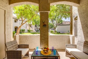 Un espacio al aire libre cubierto con mobiliario de mimbre y una mesa con una cesta de frutas y bebidas.