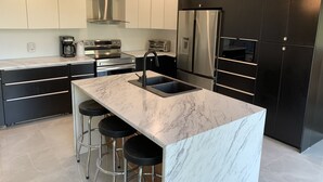 Una cocina moderna con una isla de mármol, gabinetes negros, electrodomésticos de acero inoxidable y taburetes de bar.
