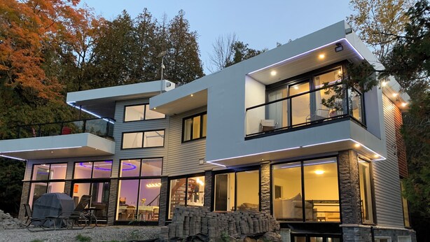 Una casa moderna de dos pisos con ventanas amplias, un balcón y fachada de piedra.