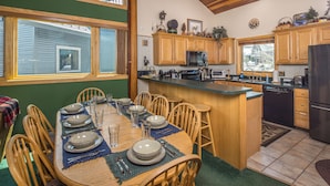 Una cocina luminosa con armarios de madera, una isla central con taburetes de bar y una mesa de comedor preparada para seis personas.